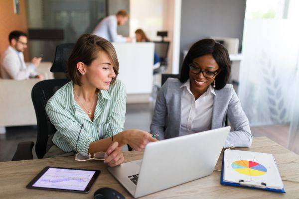 Two women sitting at a table looking at laptop computer