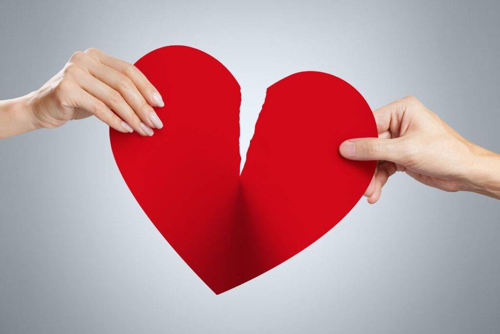 Man and Woman hands holding a red paper heart. They are ripping it apart.