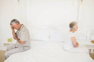 Elderly man and woman sitting on opposite sides of the bed facing away from each other