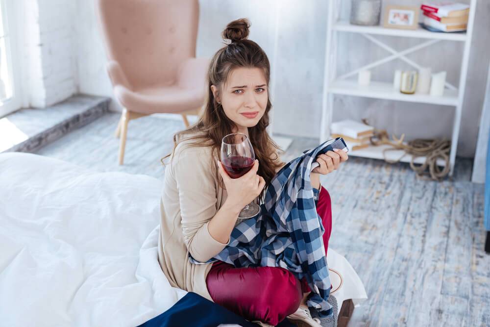 Women sitting on bed holding a glass of wine and a man's shirt