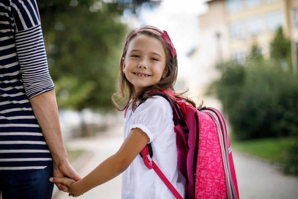 Mom holding a girls hand. Girl is smiling.