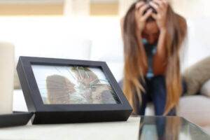 Woman crying on bed next to a broken frame that has a couple photo in it