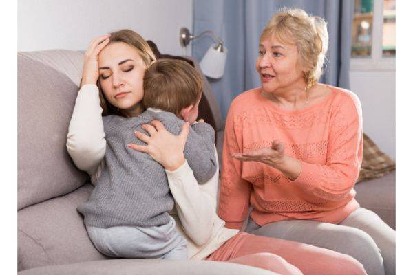 Three generations sitting on couch. Grandmother talking to daughter, daughter is upset while holding her son.