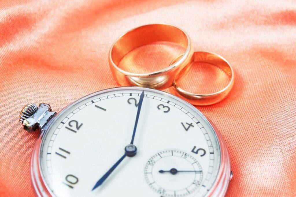 Wrist watch on table with two wedding rings next to it.