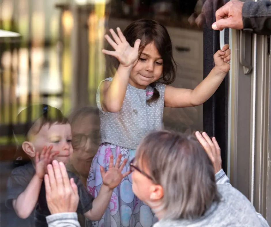a girl together with his brother greets their visiting grandmother through a glass door
