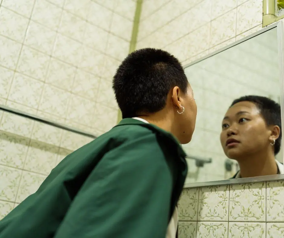 a girl experiencing gender identity issues is looking at the mirror.