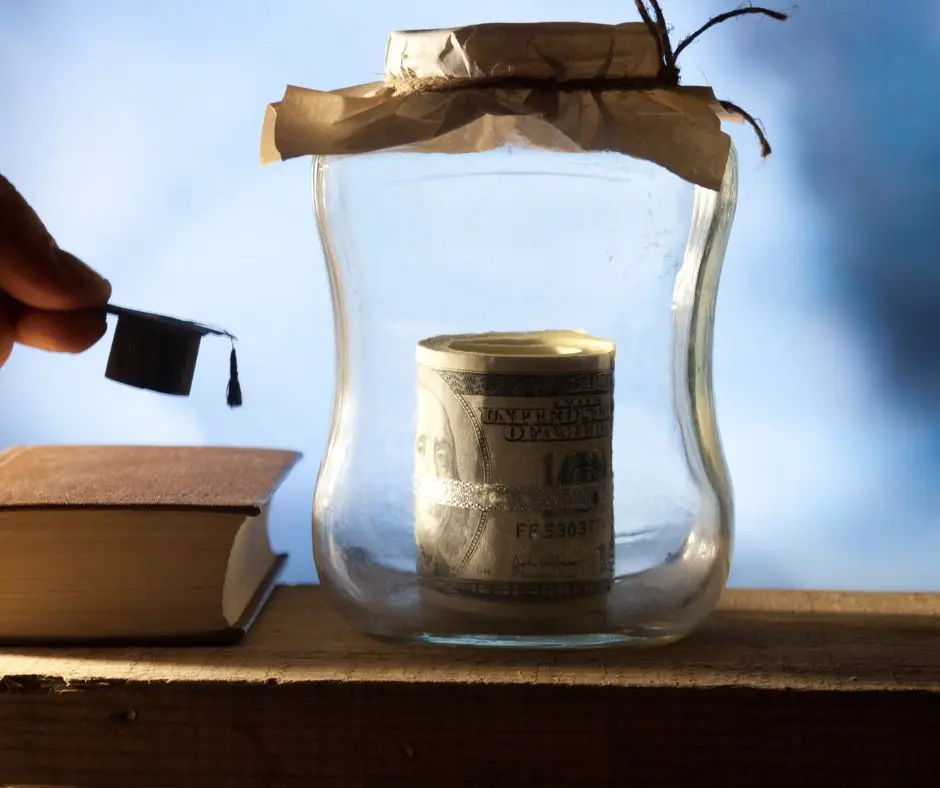 who pays for college: a small graduation cap is being placed on top of a book and beside it is a jar with dollar bills